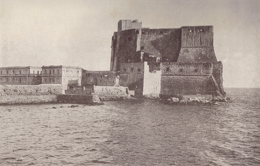 A black and white photograph, of the Castel del Ovo, with the ocean washing its base.