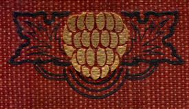 Decorated Adornment from the spine of the book, of a gilt berry with leaves in black around it on a burgundy woven ground.